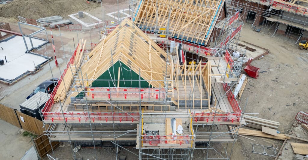 Chantier de maisons résidentielles avec charpentes en bois apparentes, échafaudages, fondations béton et équipements de construction.