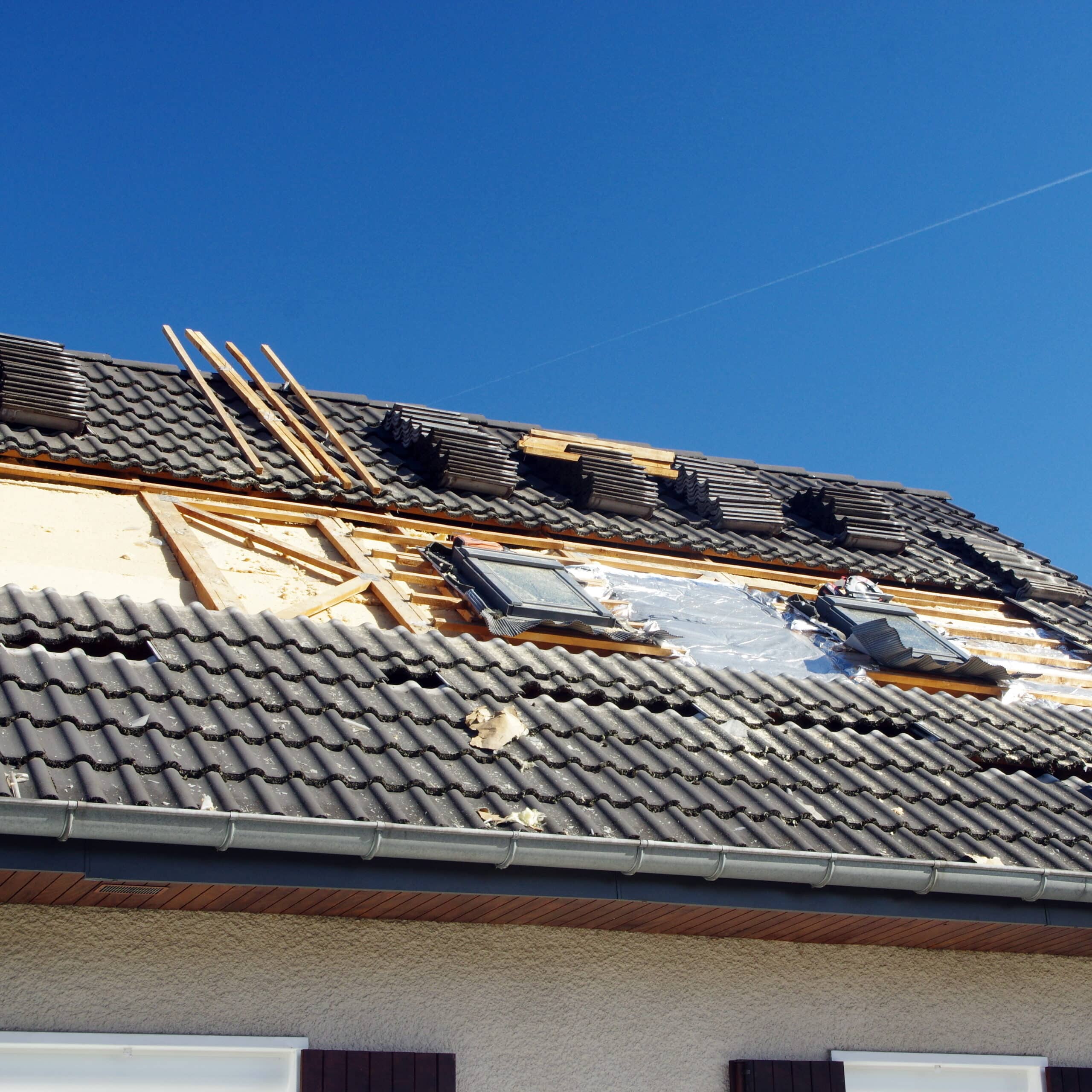 Rénovation de toiture : tuiles gris foncé, charpente apparente, isolation et deux fenêtres de toit sous un ciel bleu clair.